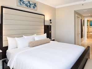 A hotel room with a large bed, a nightstand, a wall-mounted lamp, and a painting above the bed. - Luxury 2BR Residence Overlooking Naples Bay + Pool (Naples)