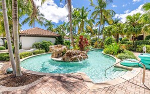 A swimming pool with a rock feature and palm trees. - Luxury 2BR Residence Overlooking Naples Bay + Pool (Naples)