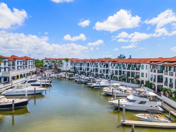 A marina with multiple boats docked, surrounded by buildings with red-tiled roofs. - Luxury 2BR Residence Overlooking Naples Bay + Pool (Naples)