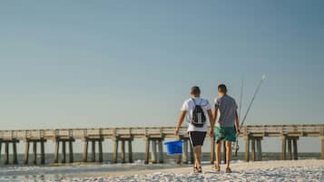 Two people walking on a sandy beach with a pier in the background.