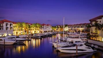 A marina with boats docked, surrounded by buildings with red roofs and palm trees.