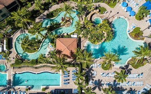 Un grand complexe hôtelier doté de plusieurs piscines, avec différents espaces de baignade, entouré de palmiers et de chaises longues.