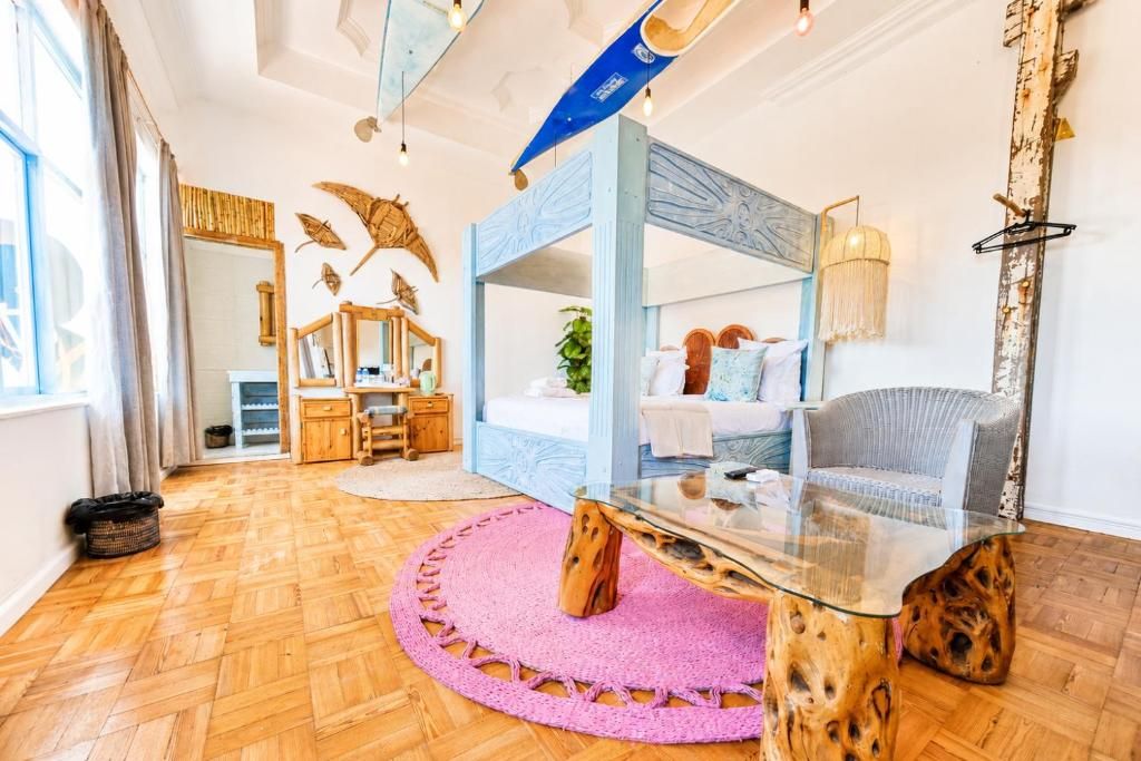 A modern bedroom with a glass coffee table, a bed with a blue headboard, a chair, and a large mirror.