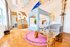 Un dormitorio moderno con una mesa de centro de vidrio, una cama con cabecera azul, una silla y un espejo grande.