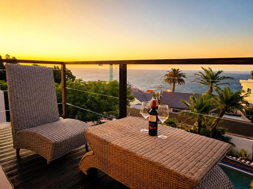 A balcony with wicker furniture and a bottle of wine, overlooking a body of water and palm trees.