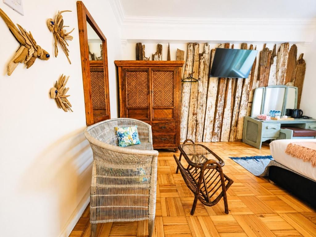 A room with a wicker chair, a wooden cabinet, a television, and a bed.