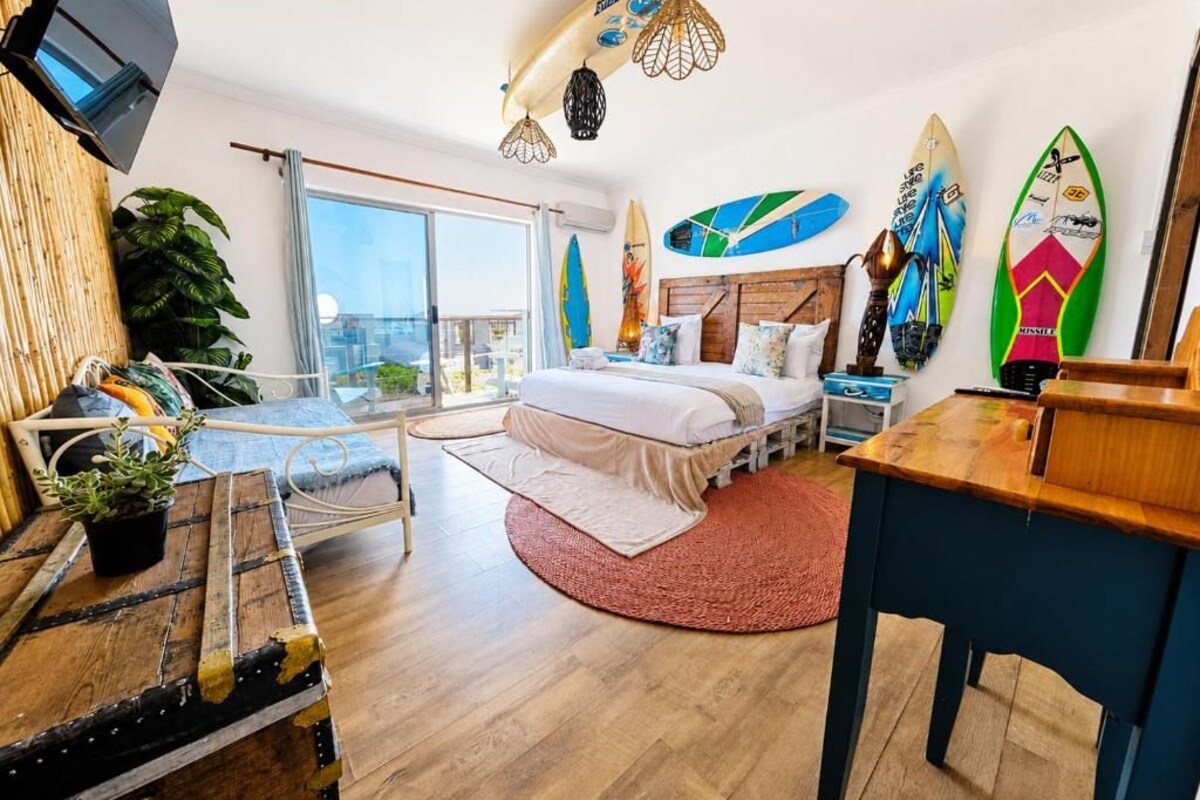 Un dormitorio moderno con cama, escritorio, televisor y tablas de surf en la pared.