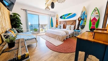 A modern bedroom with a bed, a desk, a TV, and surfboards on the wall.