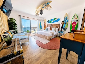 Un dormitorio moderno con cama, escritorio, televisor y tablas de surf en la pared.