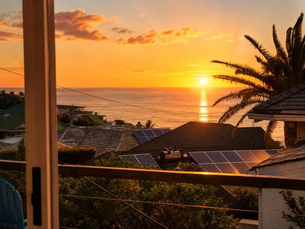 Une vue sur le coucher de soleil depuis un balcon agrémenté de panneaux solaires et d’un palmier.