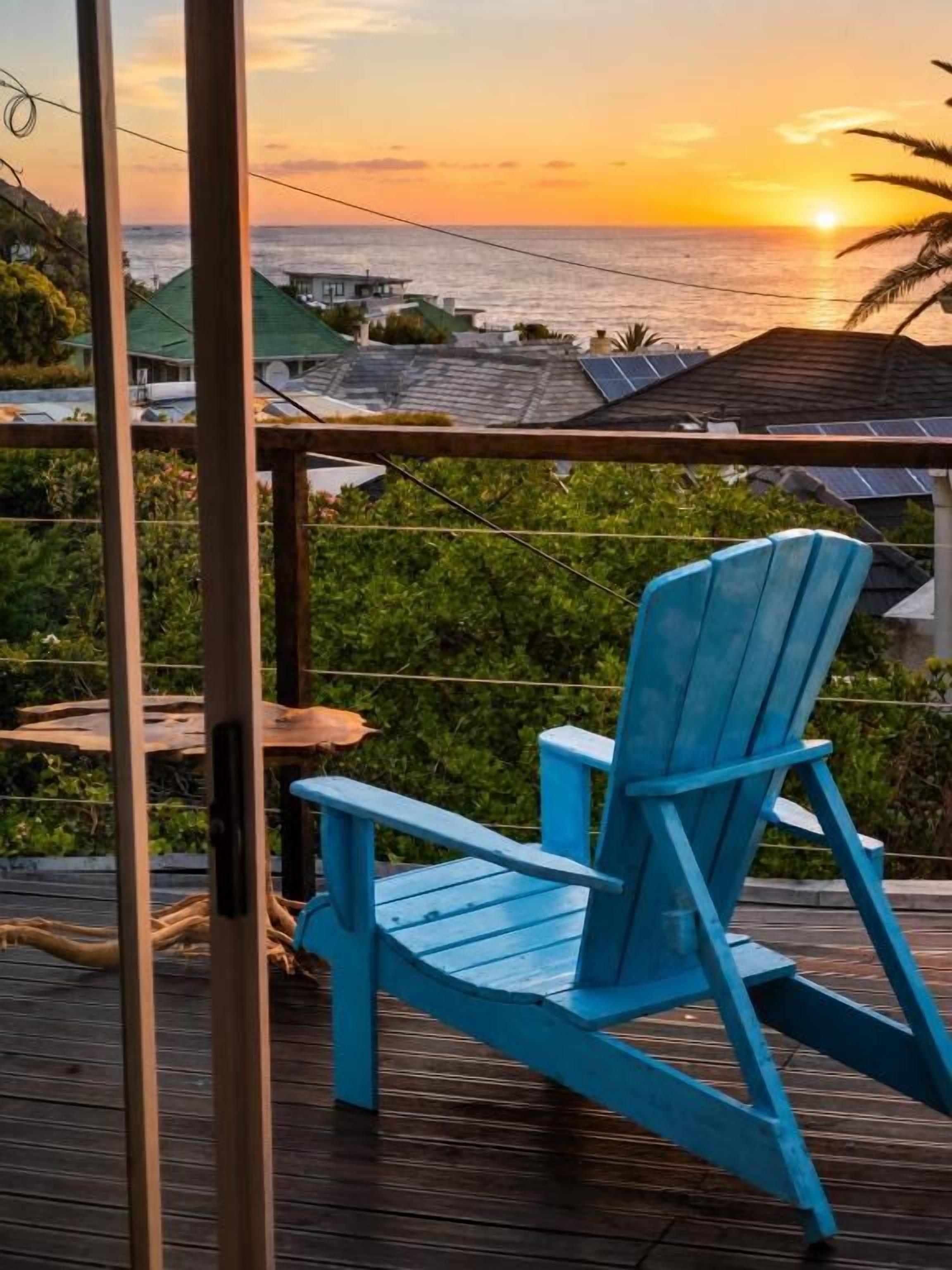 Une chaise Adirondack bleue est posée sur une terrasse en bois, d’où l’on peut admirer le coucher de soleil sur l’océan.