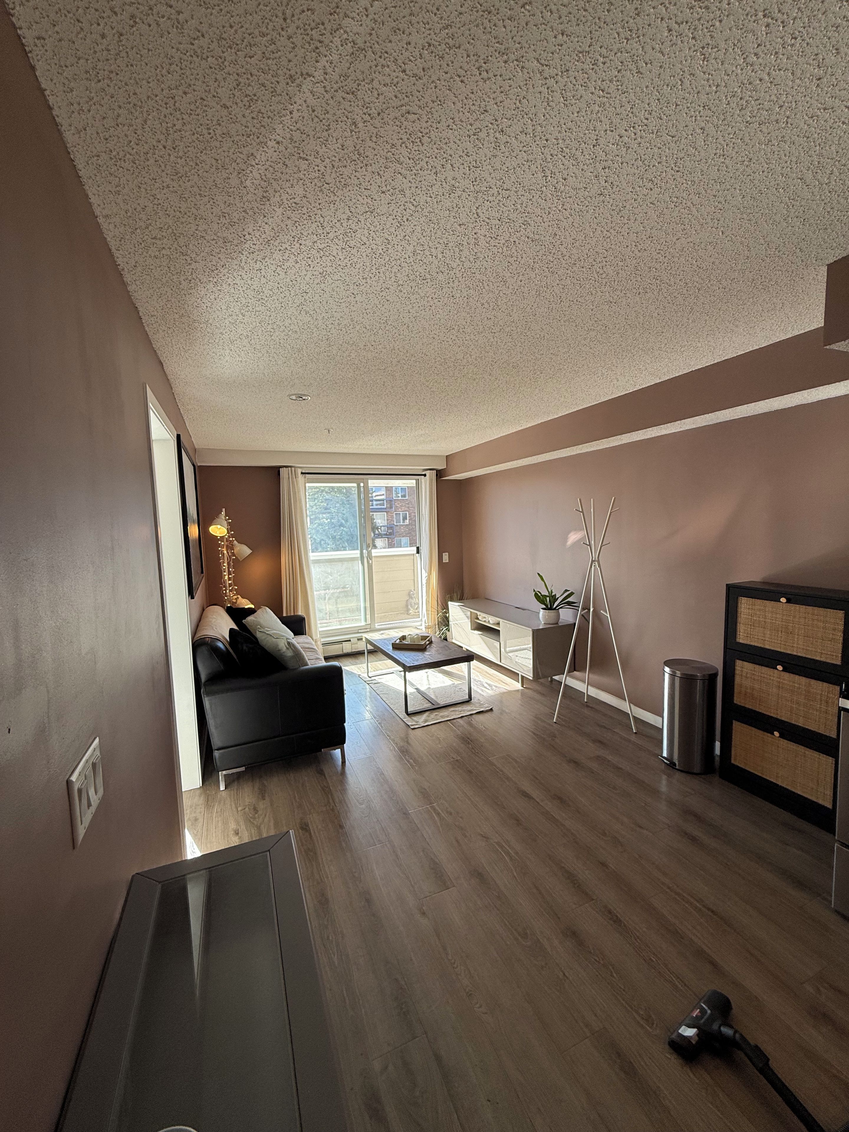 A spacious living area with a sofa, a coffee table, a TV, and a balcony with a view.
