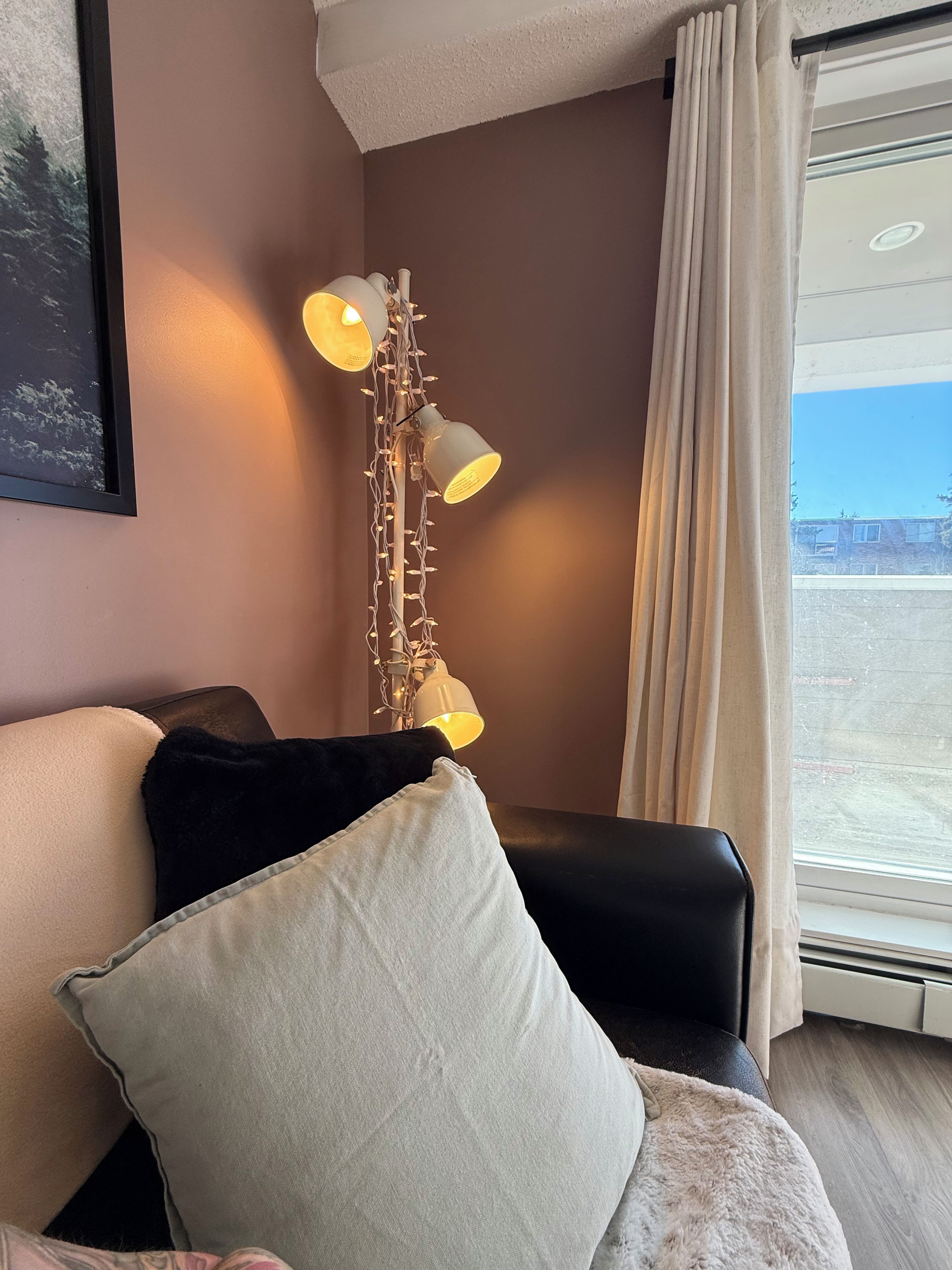 A room with a sofa, a floor lamp, and a window with curtains.