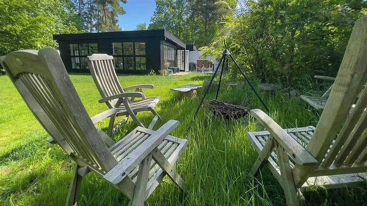A wooden deck with Adirondack chairs, a fire pit, and a modern house in the background.