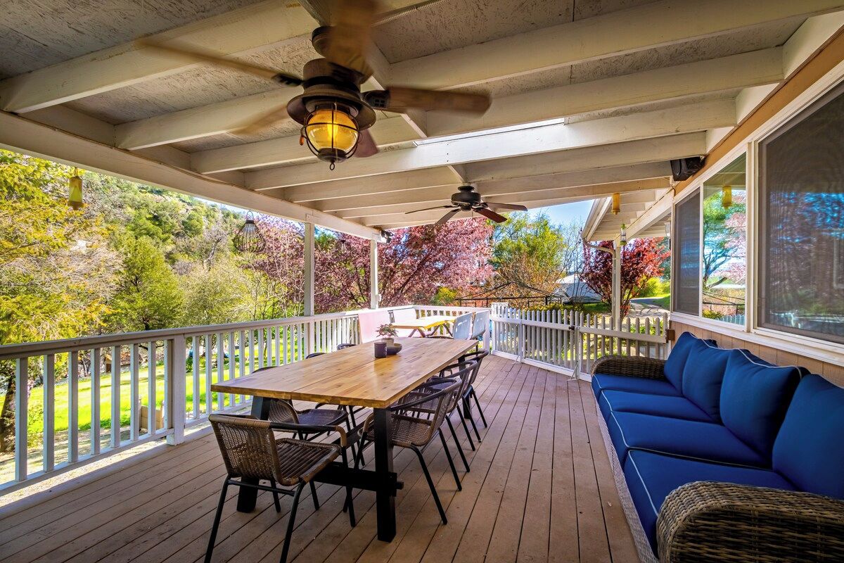 A covered outdoor deck with a wooden table and chairs, a blue sofa, and a ceiling fan.