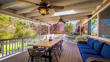 A covered outdoor deck with a wooden table and chairs, a blue sofa, and a ceiling fan.
