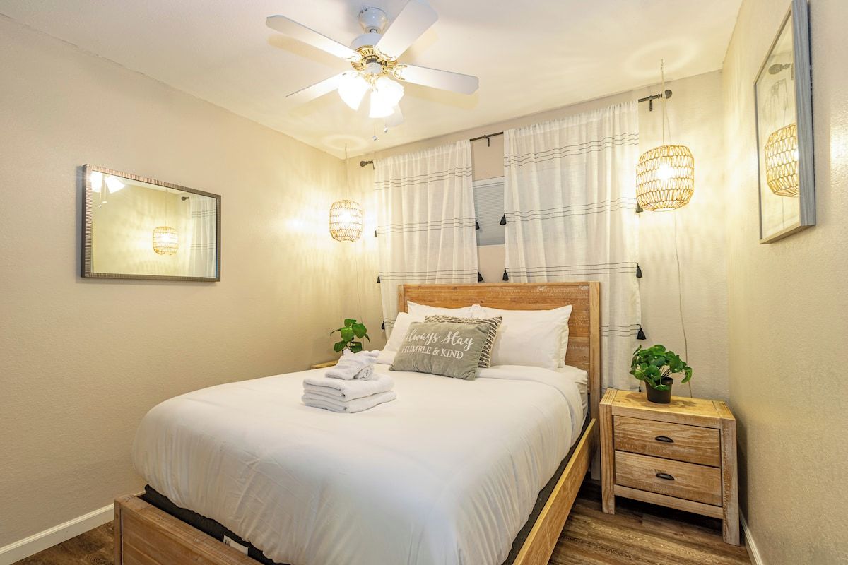 A neatly made bed with a headboard, a bedside table with a lamp, and a ceiling fan.