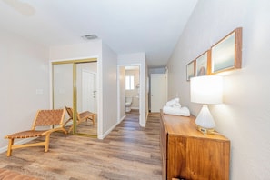 Un couloir avec un plancher en bois, un miroir, un banc en bois, une table de chevet avec une lampe et des tableaux encadrés accrochés au mur.