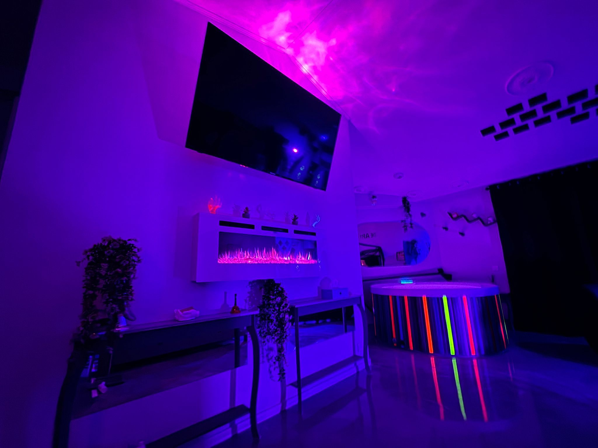 Una habitación con televisión de pantalla plana montada en la pared, chimenea y una mesa redonda con luces de neón.
