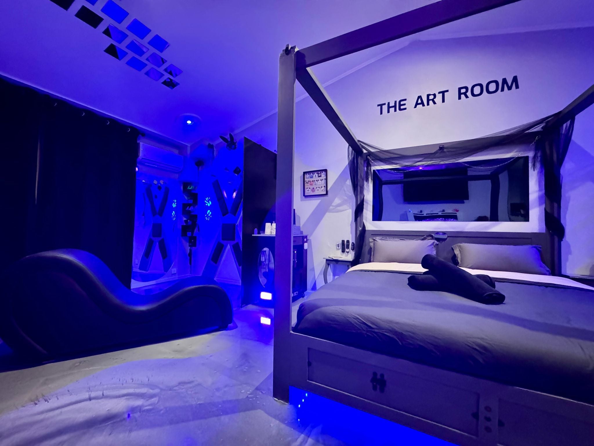Une chambre avec un lit à baldaquin, un téléviseur fixé au mur et une pancarte sur laquelle on peut lire : « L’ATELIER D’ART ».