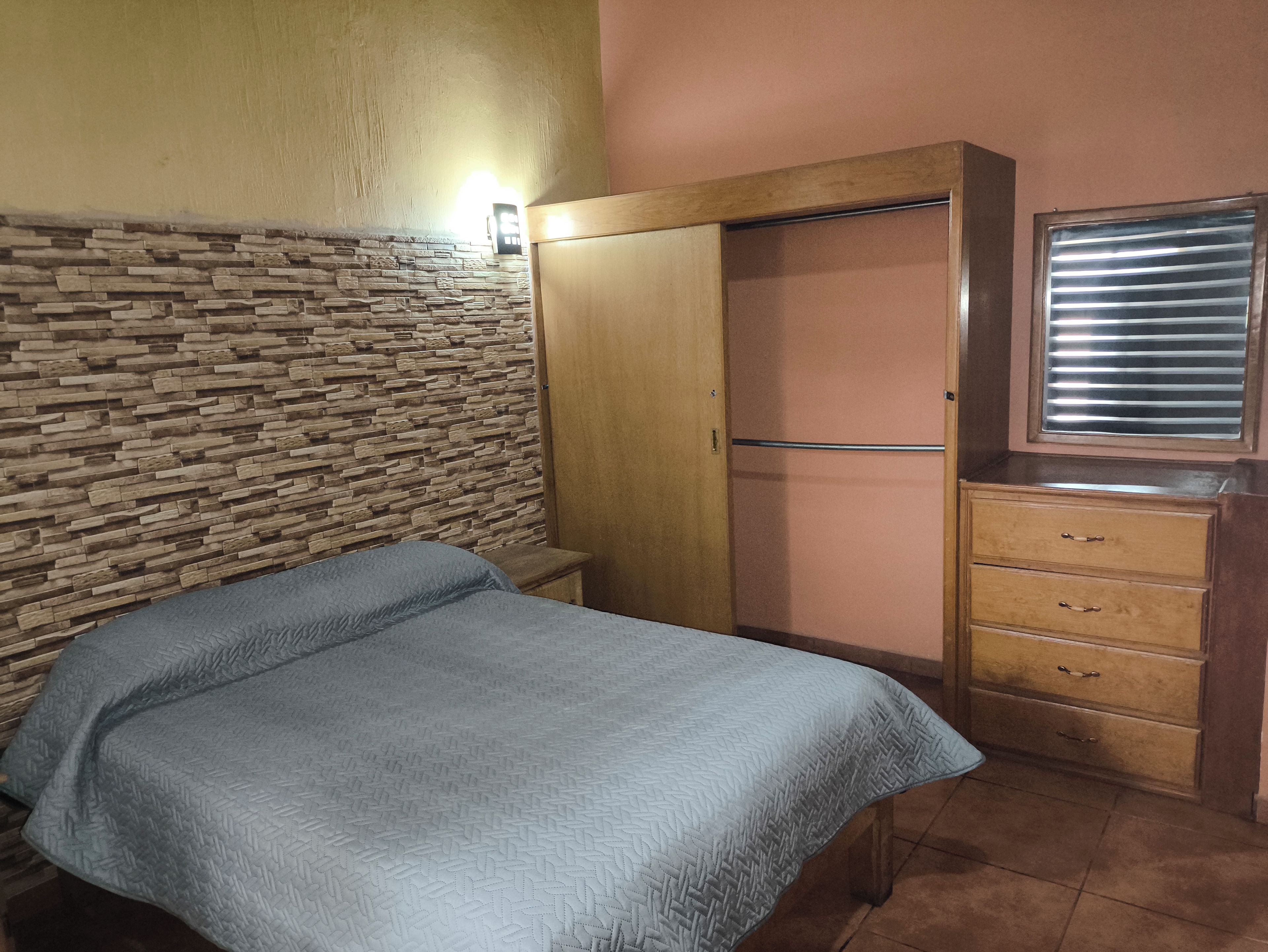 Une chambre à coucher comprenant un lit, une armoire, une commode et une fenêtre avec des stores.