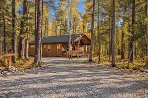 Eine Lodge mit überdachter Veranda und einem Schotterweg, umgeben von hohen Bäumen.