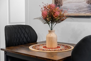Taula de dinar amb un ram de flors, una placemat amb dibuixos i cadires tapissades de color negre.