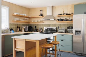 Eine moderne Küche mit einer zentralen Kochinsel, Holzbarhocker, einem Einbauofen und einem Edelstahlkühlschrank.