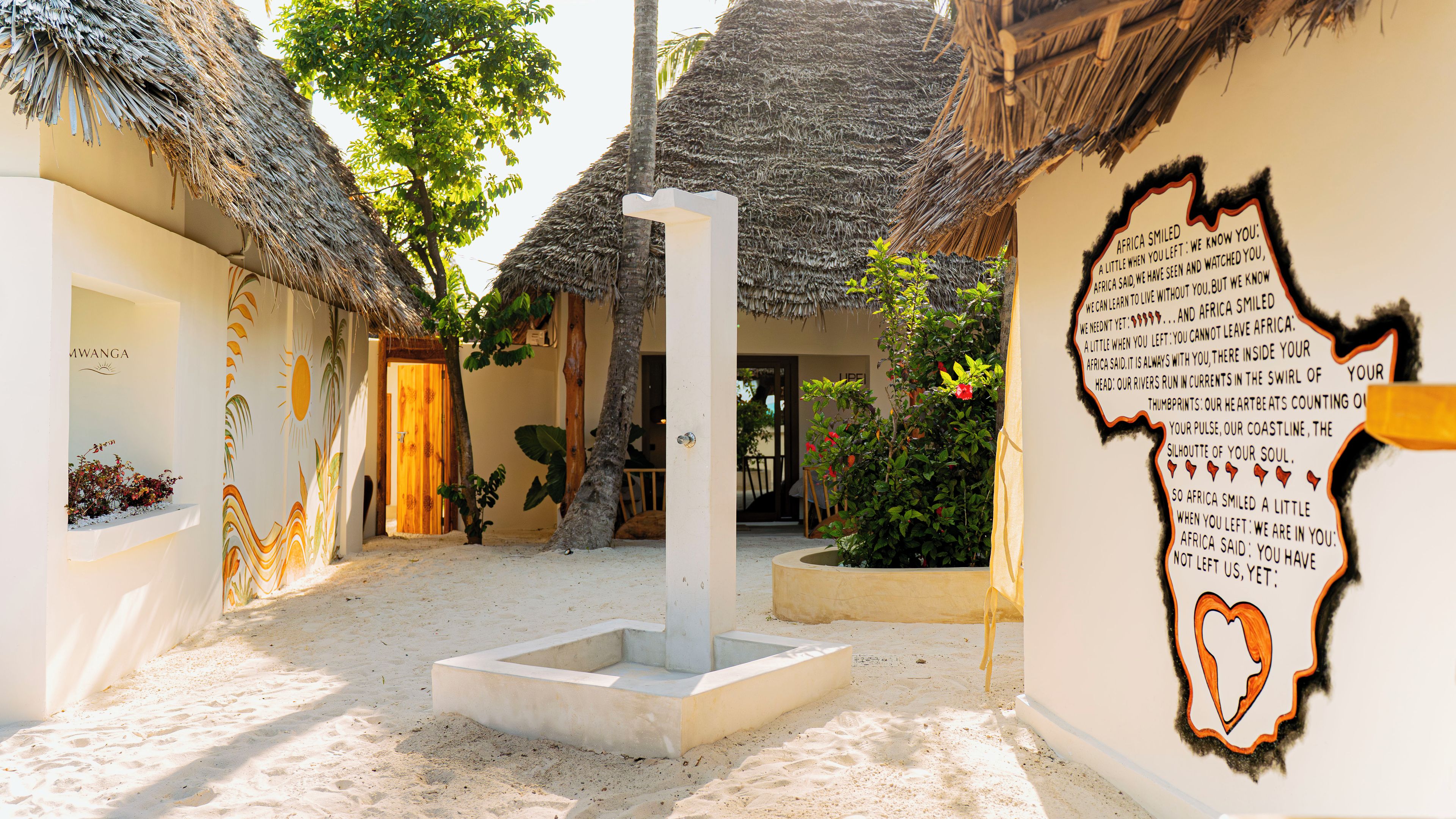 Zona en la playa con construcciones de techo de paja, un pilar central y una pared con un recorte en forma de corazón.