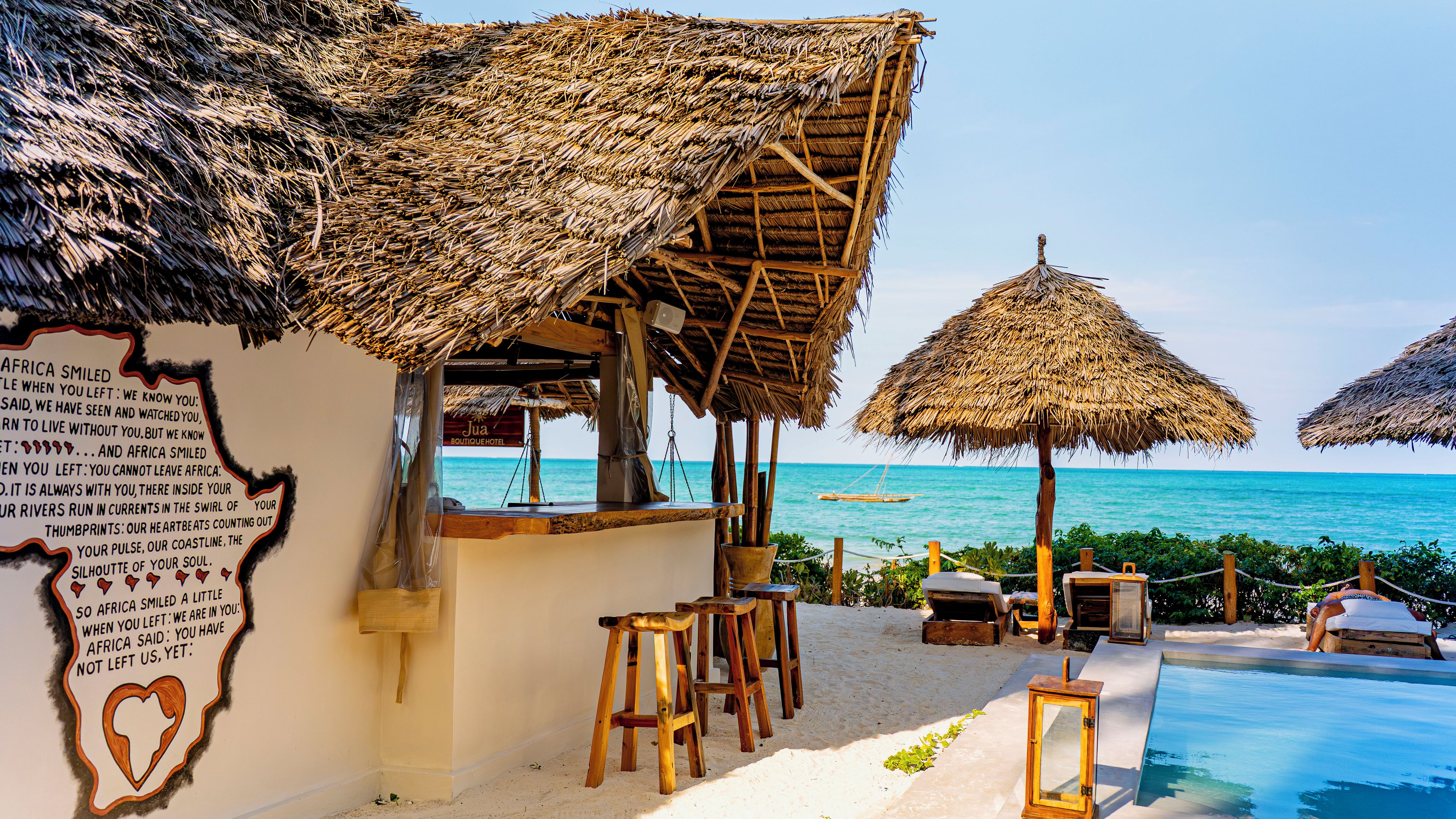 Un resort frente a la playa con sombrillas de paja, una piscina y un letrero con forma de corazón.