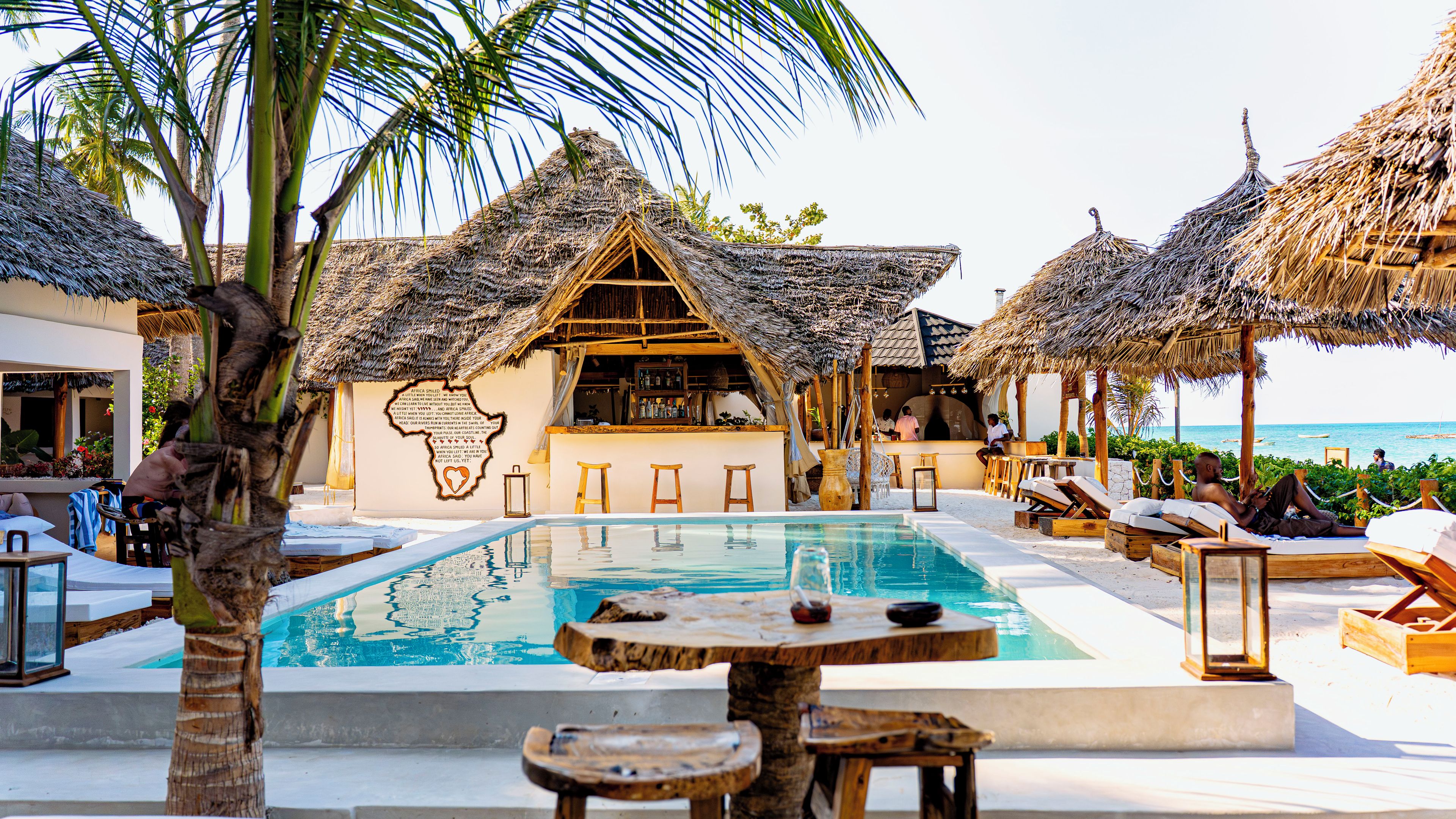 A poolside area with thatched-roof structures, a bar, and lounge chairs.