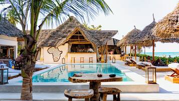A poolside area with thatched-roof structures, a bar, and lounge chairs.