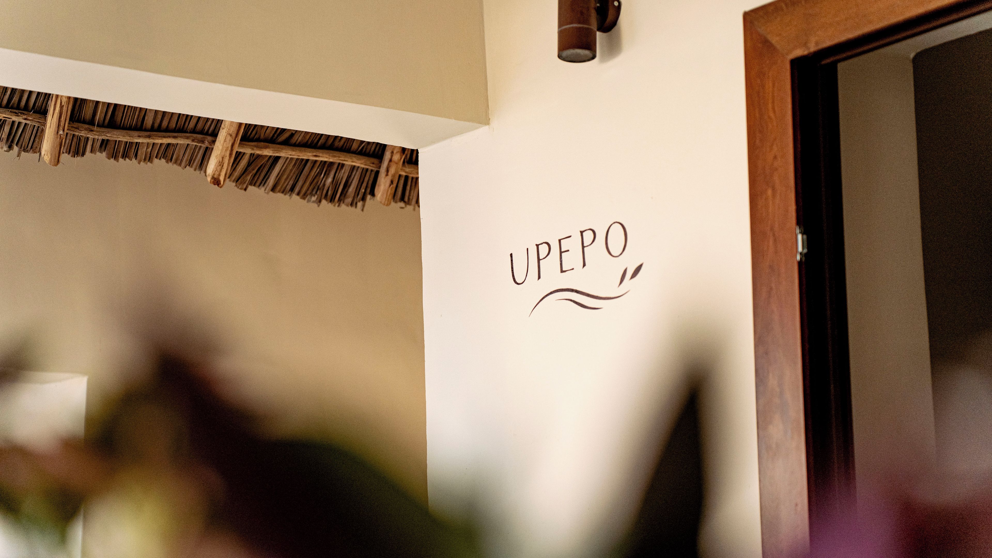 Un mur sur lequel est inscrit le mot « UPEPO » et un plafond en chaume.