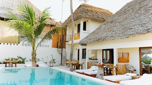 A poolside area with a thatched-roof building, lounge chairs, and a small table. - Jua Boutique Hotel (Jambiani)