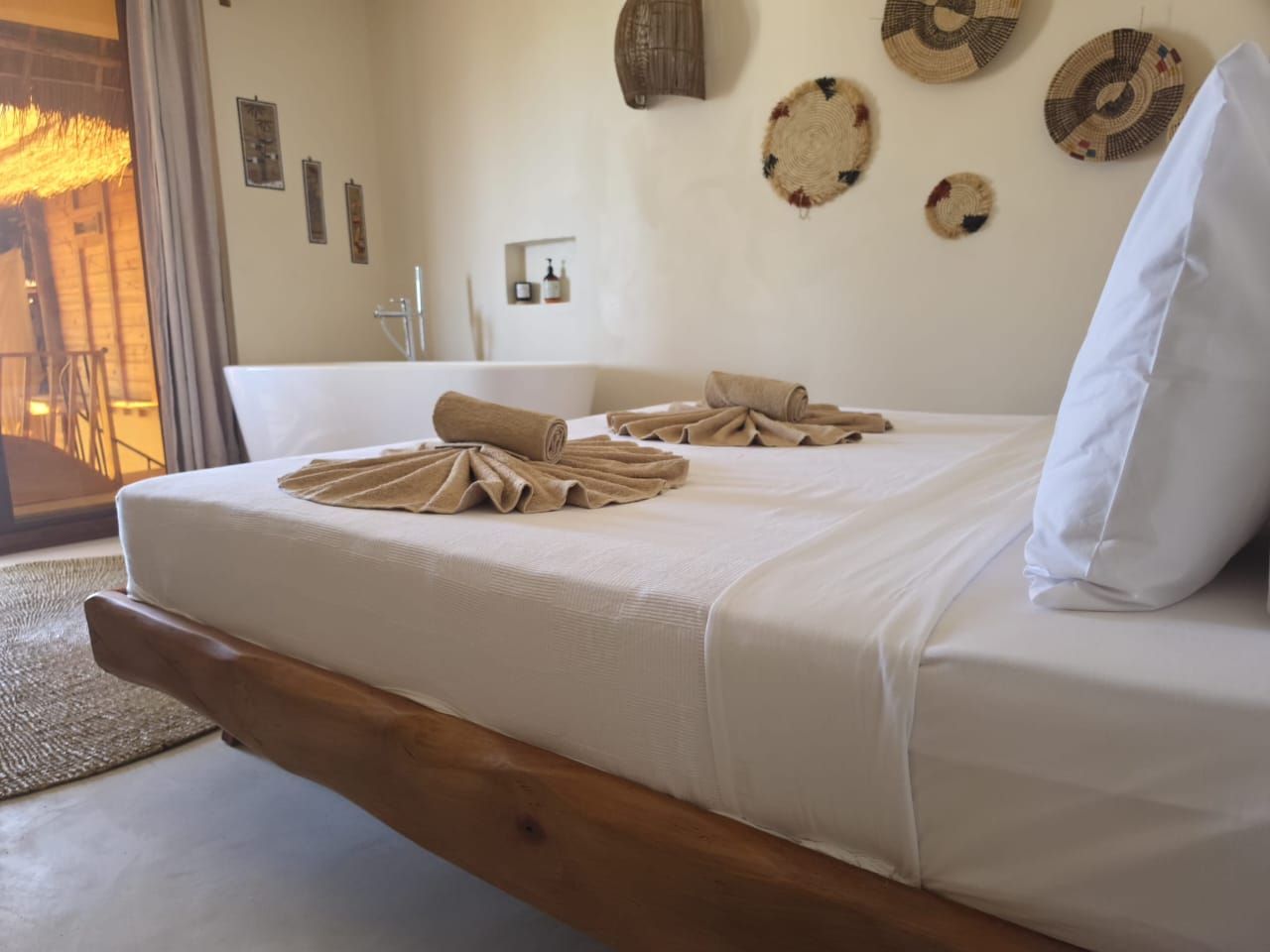 Una cama con estructura de madera, ropa de cama blanca y toallas dispuestas encima.