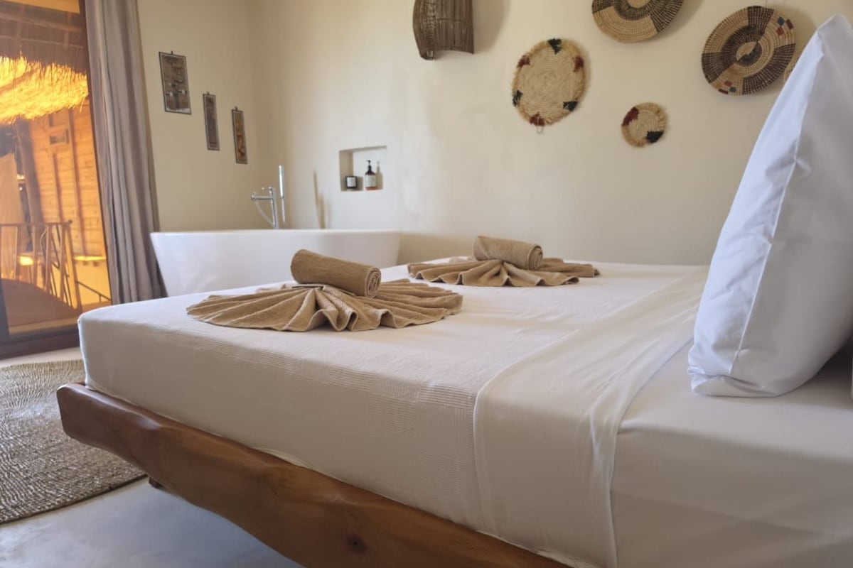 A bed with a wooden frame, white bedding, and towels arranged on it.