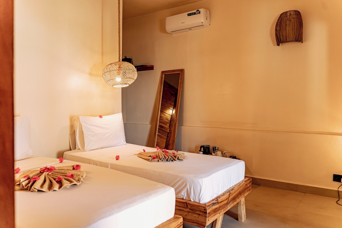 A hotel room with two beds, a large mirror, an air conditioning unit, and a wooden bench.