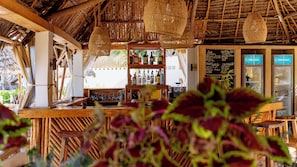 A bar area with a wooden counter, shelves of bottles, and a chalkboard menu. - Jua Boutique Hotel (Jambiani)