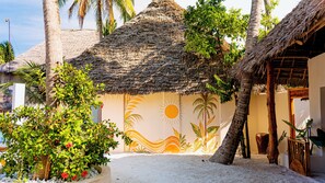 A beachside building with a thatched roof, surrounded by palm trees and a sandy ground. - Jua Boutique Hotel (Jambiani)