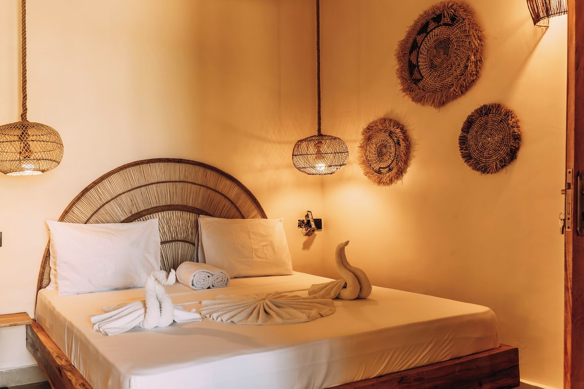 A bed with a woven headboard, white linens, and a towel arrangement.