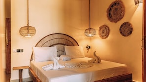 A bed with a woven headboard, white linens, and a towel arrangement. - Jua Boutique Hotel (Jambiani)