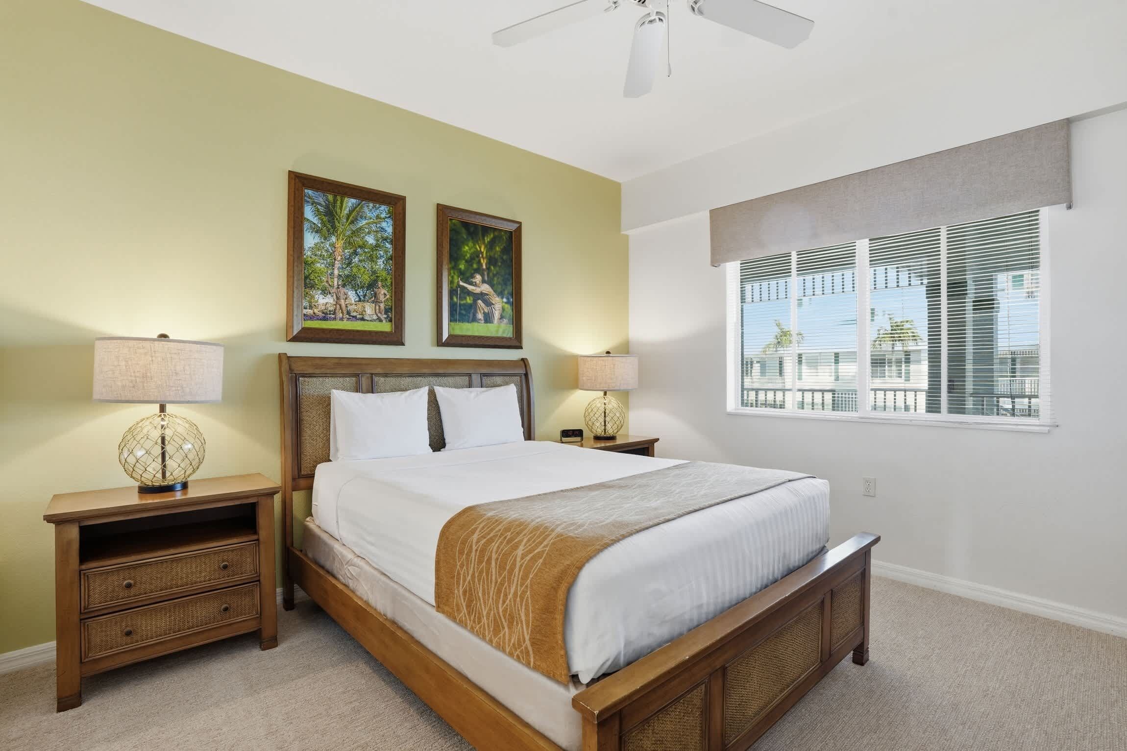 A hotel room with a large bed, two nightstands, a ceiling fan, and a window with blinds.