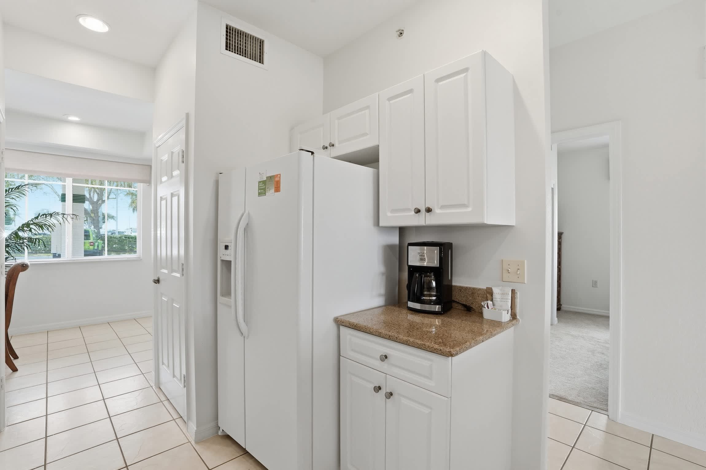 A modern kitchen with white cabinetry, a built-in refrigerator, and a coffee maker on the countertop.