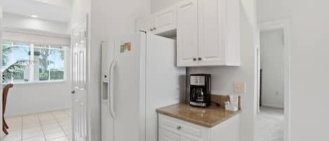 A modern kitchen with white cabinetry, a built-in refrigerator, and a coffee maker on the countertop.