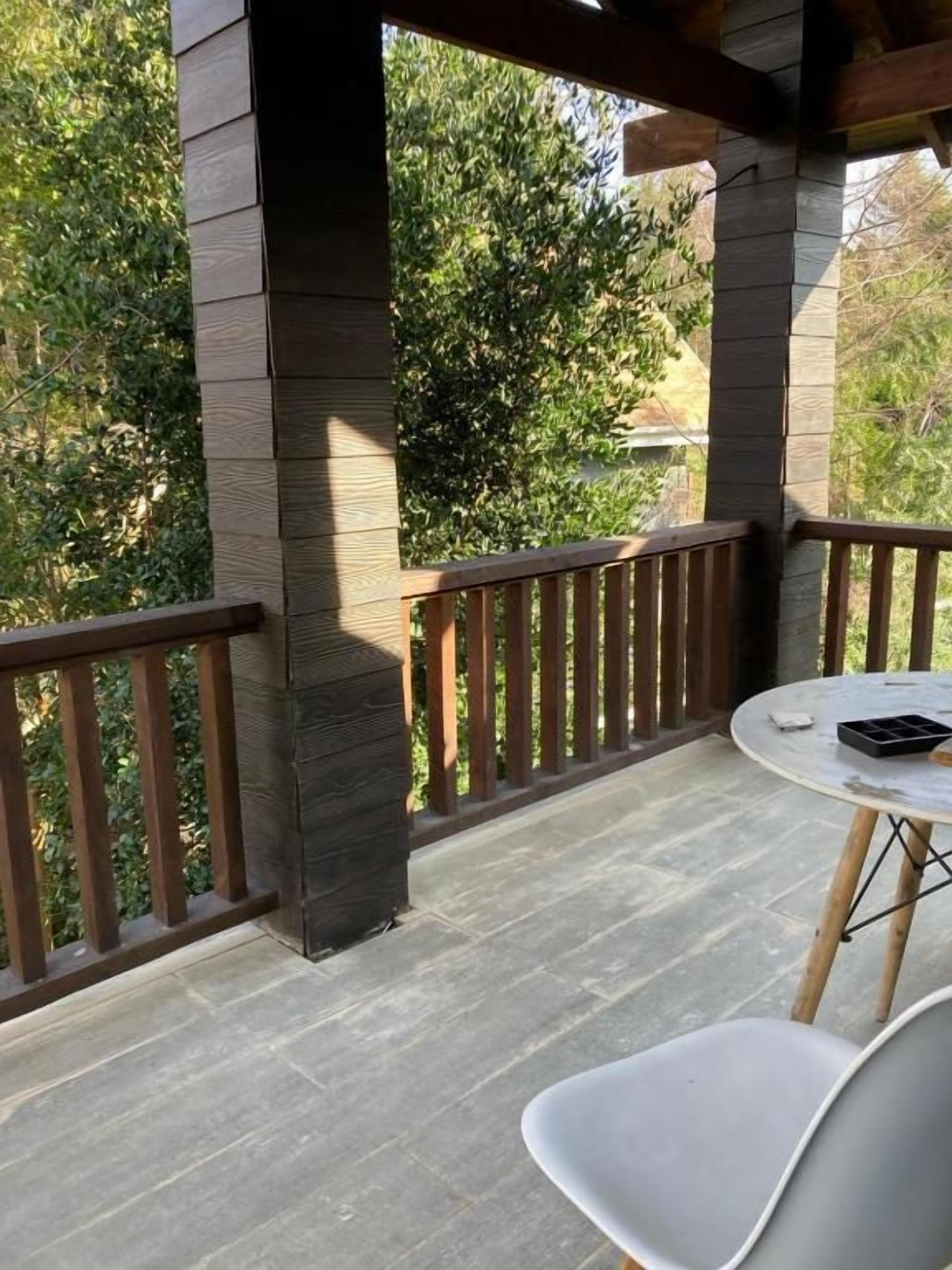 A covered outdoor area with a wooden railing, a round table, and a white chair.