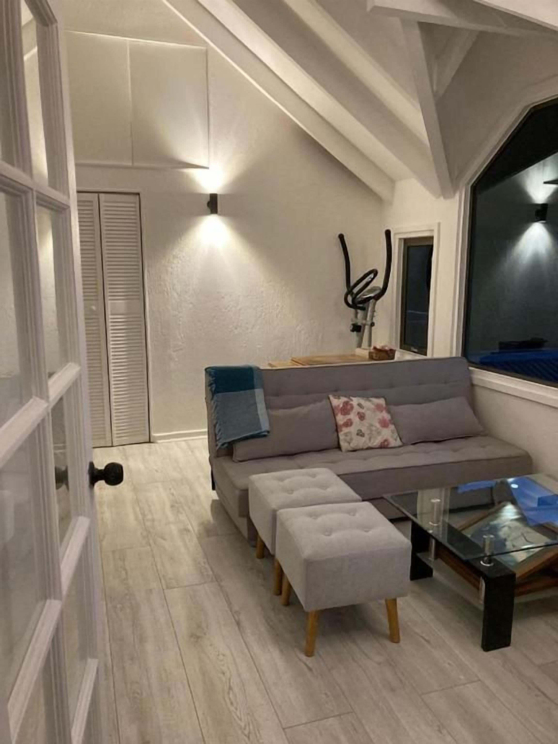 A modern living room with a grey sofa, a glass coffee table, and a large window.