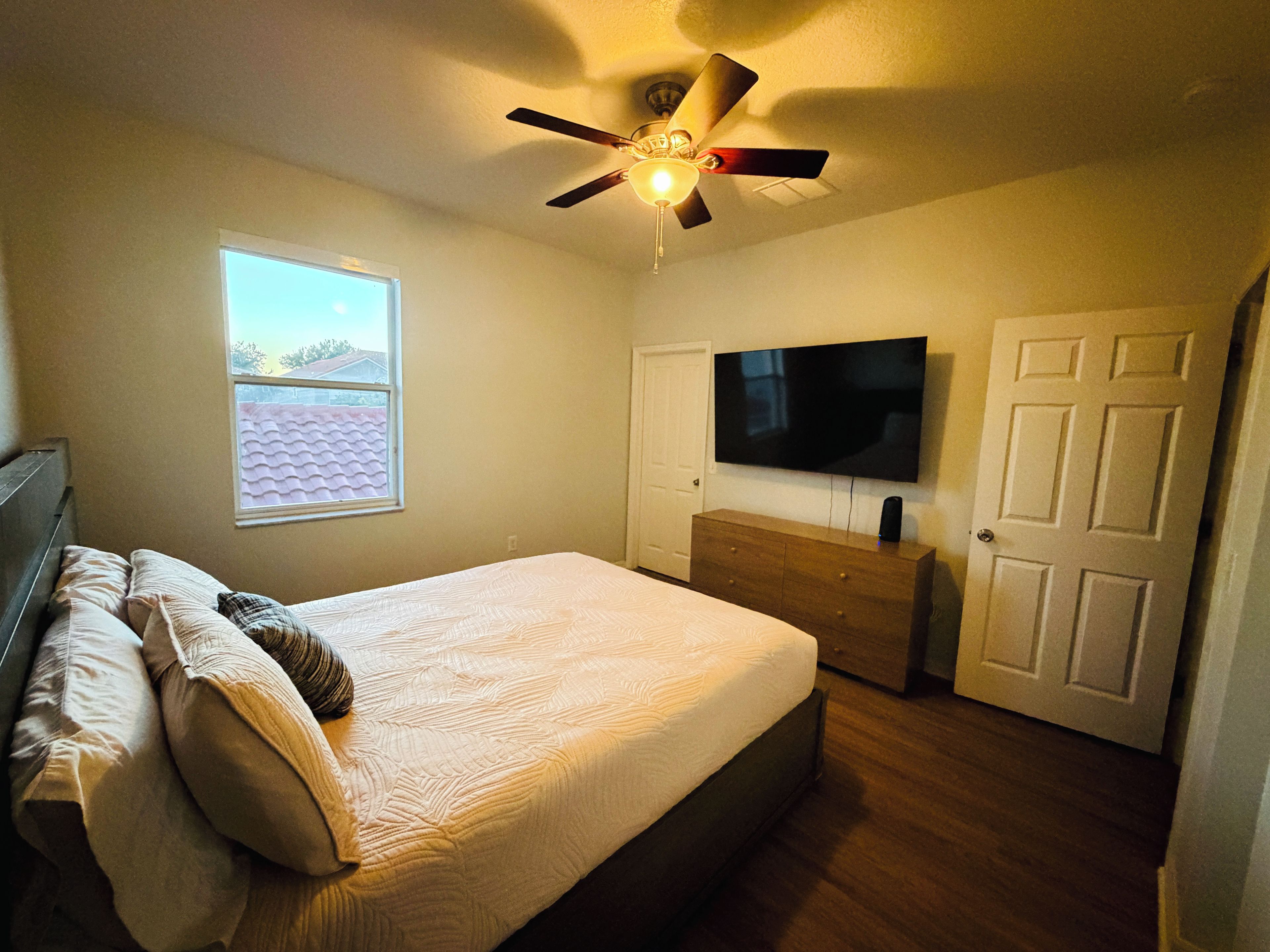 Quarto com cama, ventilador de teto, televisão e cômoda.