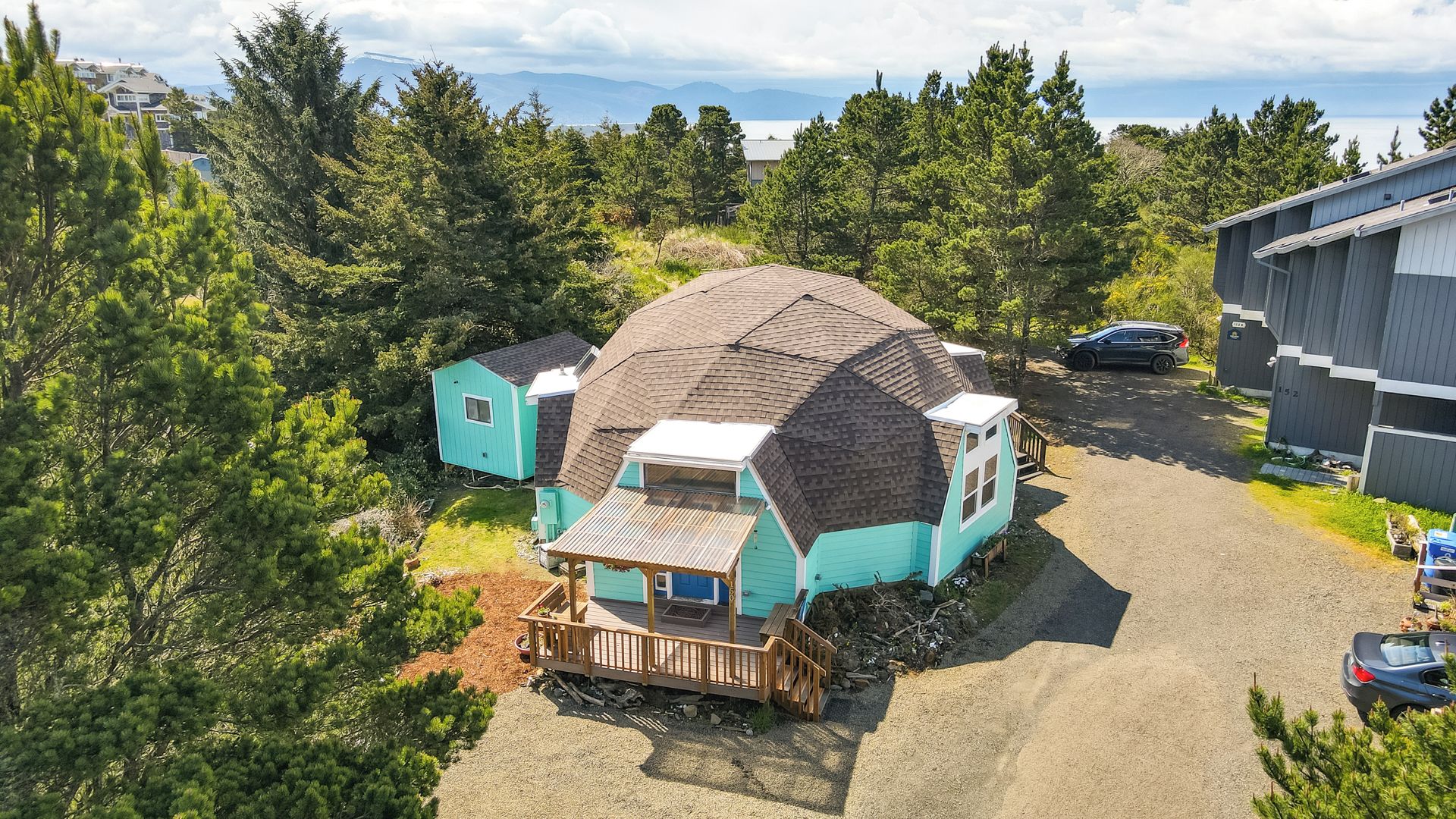 Ein kleines, eingeschossiges Haus mit Satteldach, einer Holzterrasse und einer Zuwegung mit Kies.