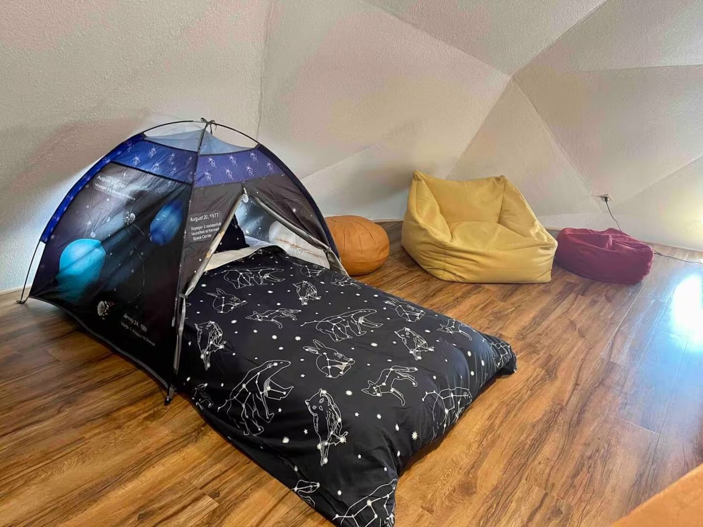 A tent-like structure with a space-themed design, a bean bag chair, and a small orange ball on a wooden floor.