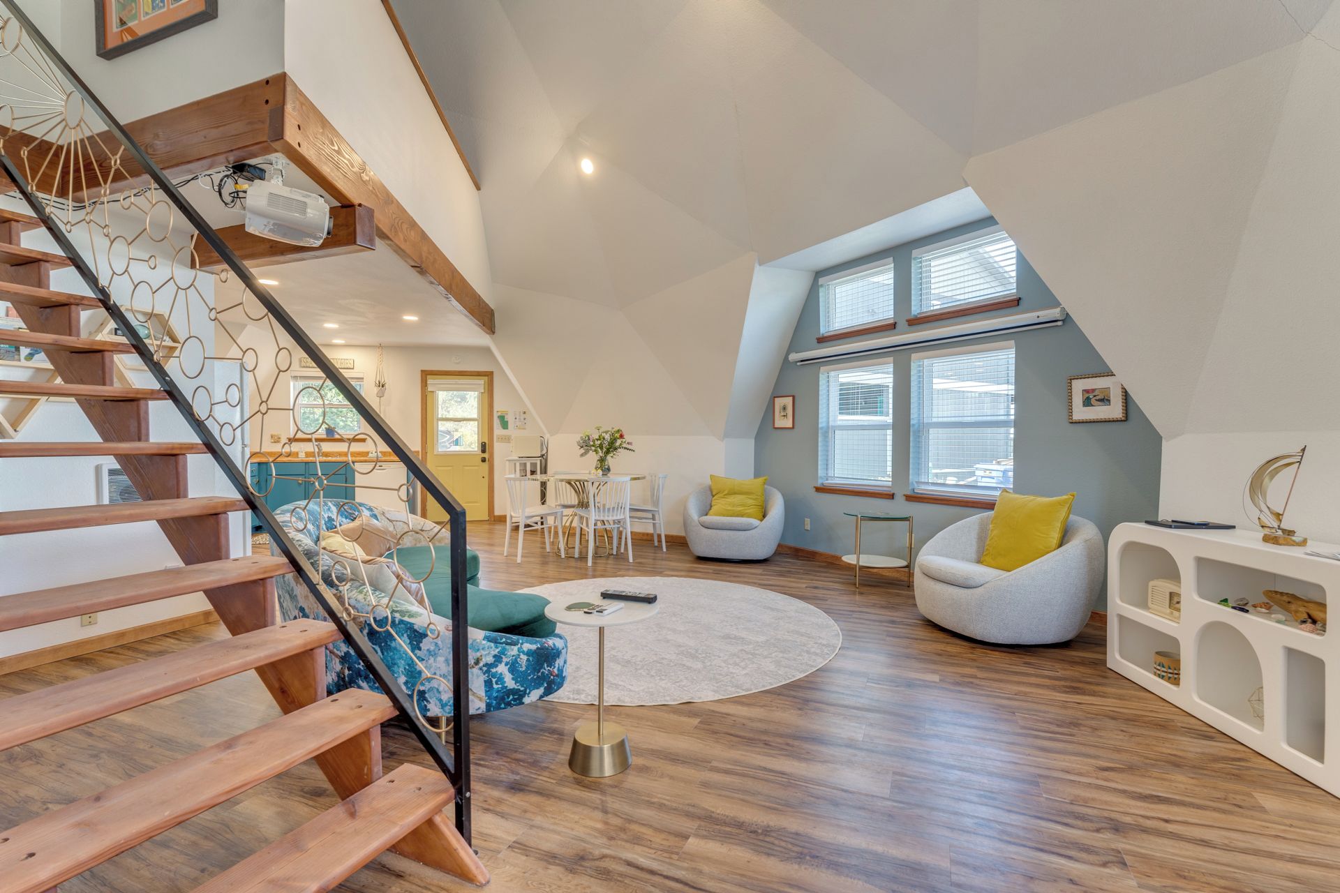 A spacious loft with a wooden staircase, a round coffee table, and a seating area with armchairs.